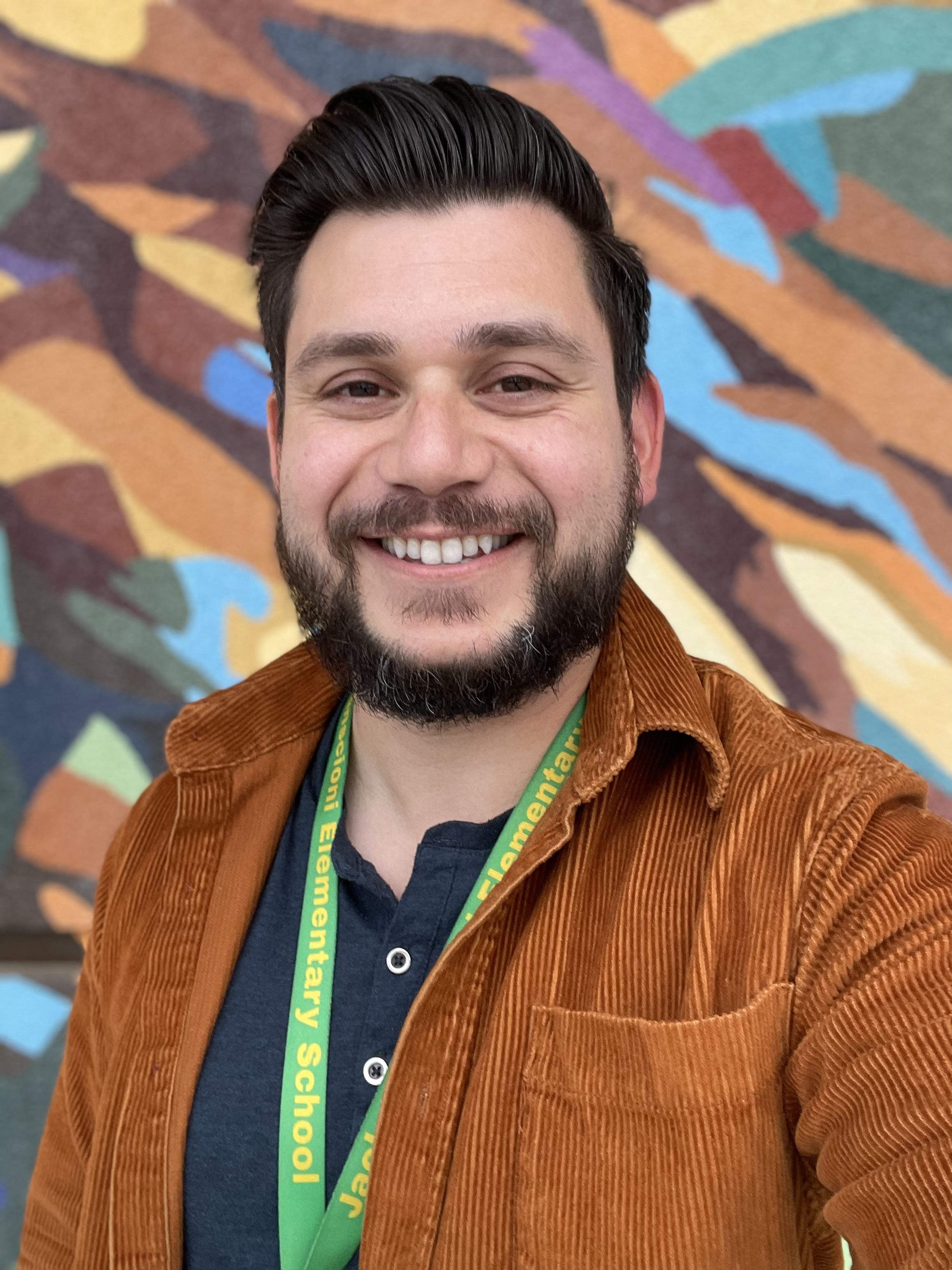 Mr. Firme smiling in front of a colorful mural